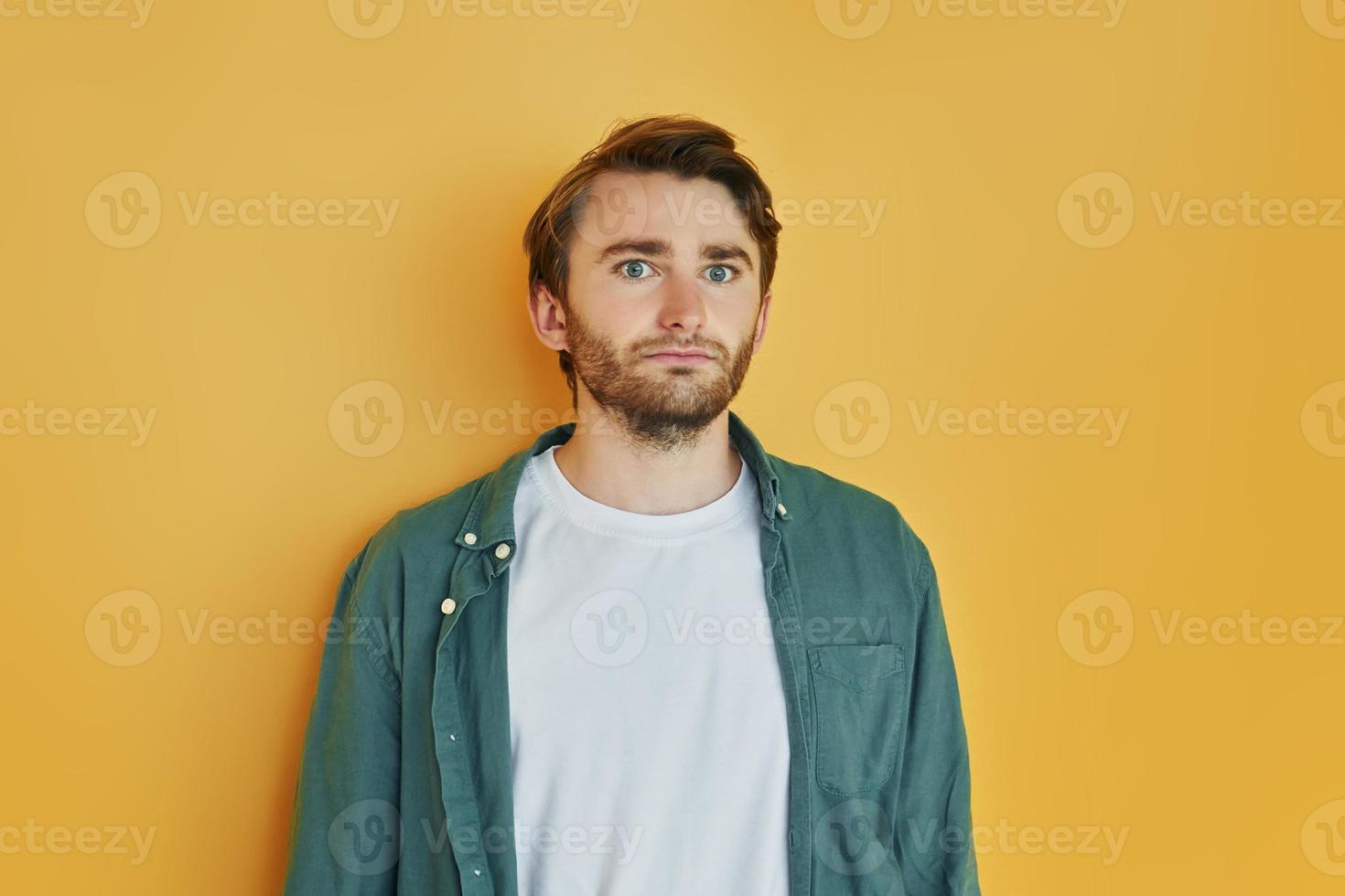 Posing for the camera, different emotions. Young man in casual clothes standing indoors in the studio photo