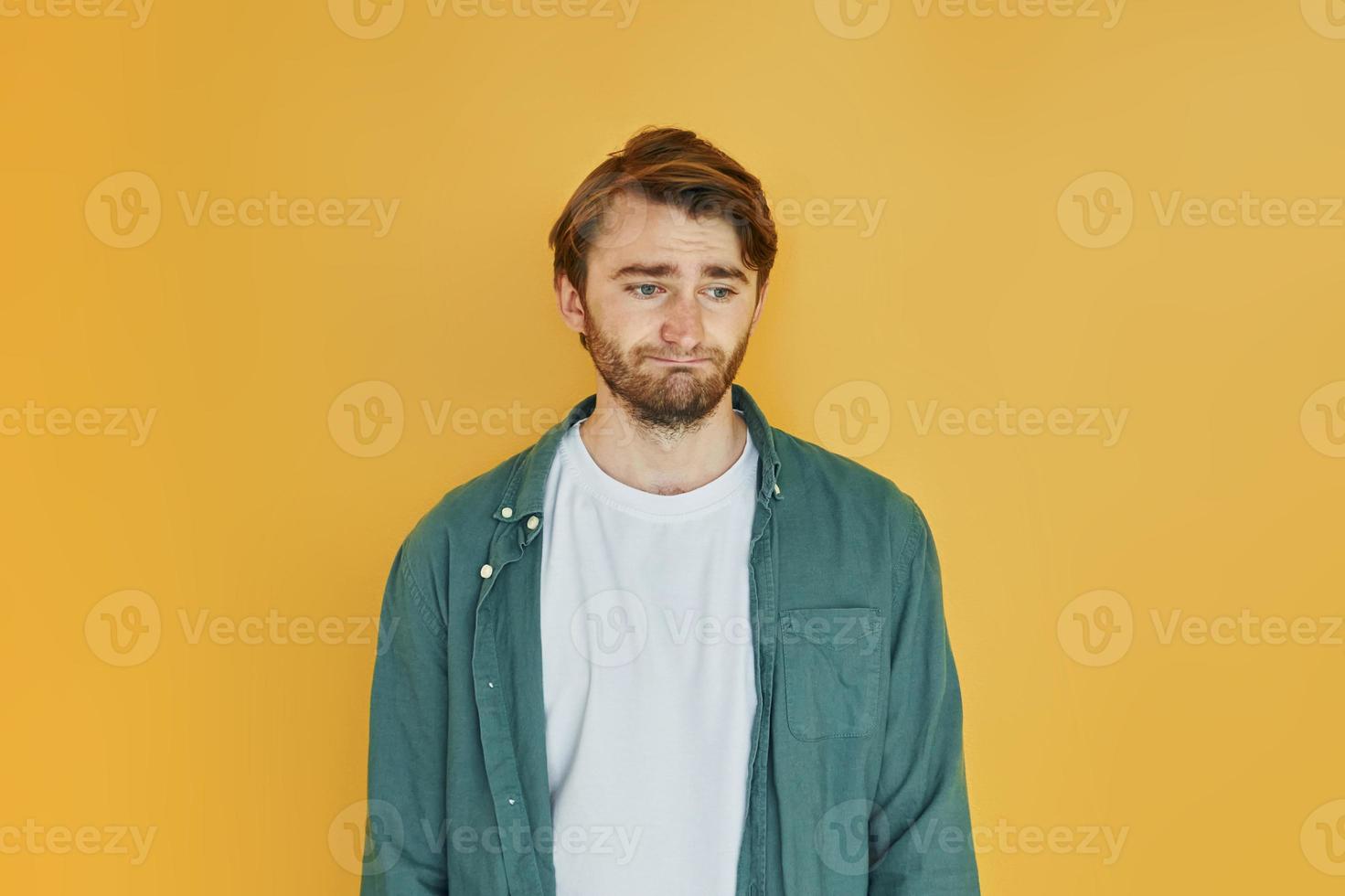 Young man in casual clothes standing indoors in the studio and demonstrates emotions photo