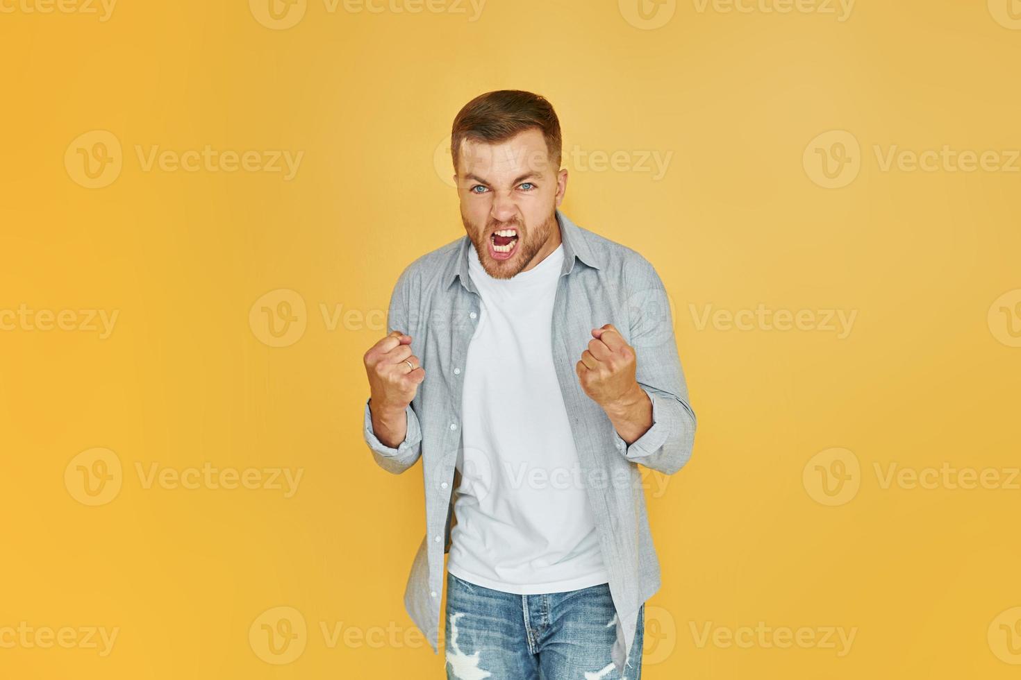 Fells anger. Young man in casual clothes standing indoors in the studio photo