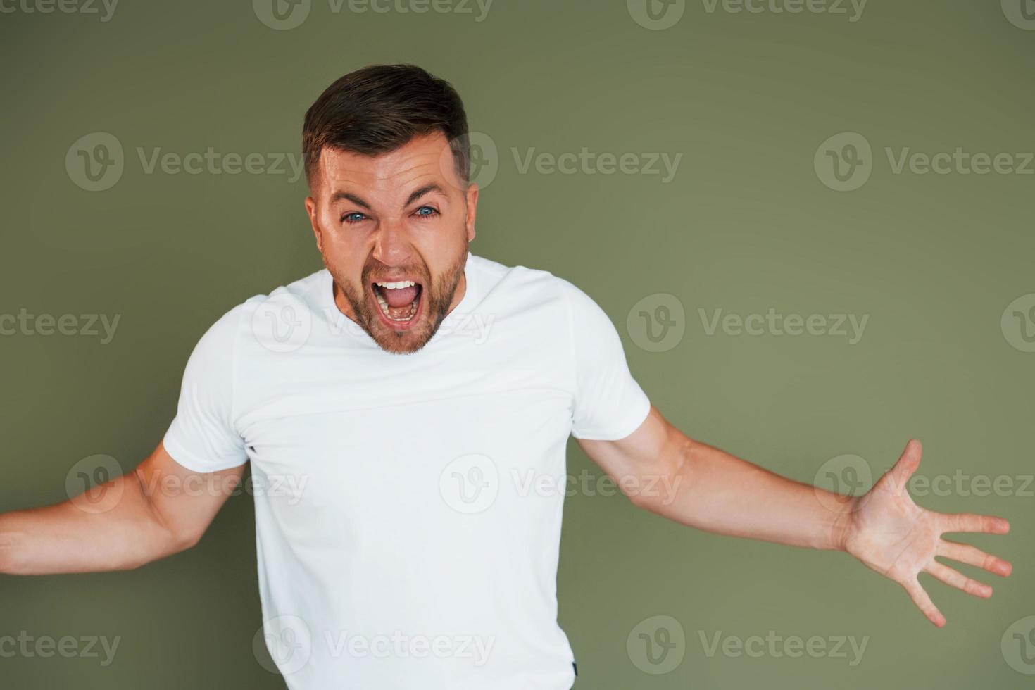 Angry young man in casual clothes standing indoors in the studio photo