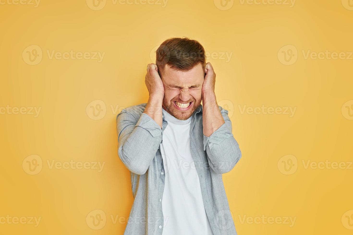 Headache and anger. Young man in casual clothes standing indoors in the studio photo