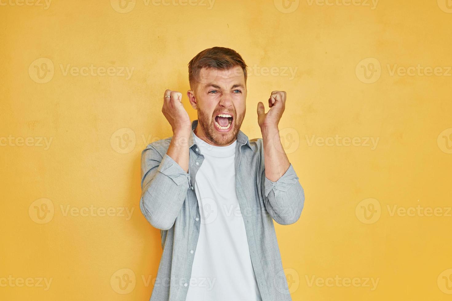 Headache and anger. Young man in casual clothes standing indoors in the studio photo