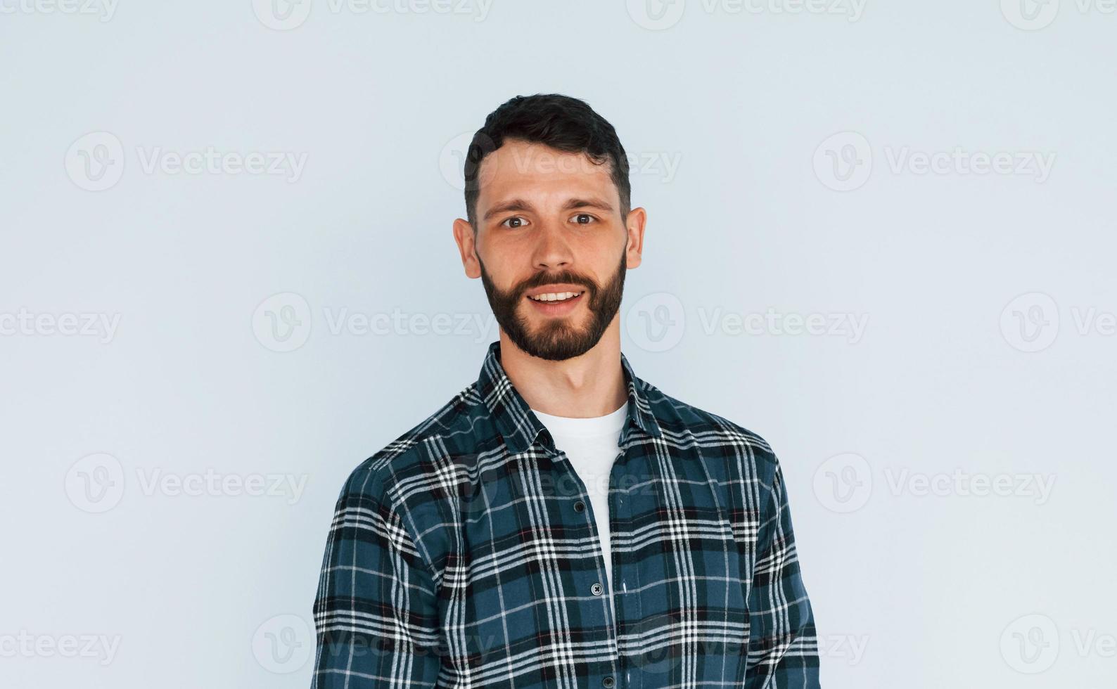 In in a plaid shirt. Young man in casual clothes standing indoors in the studio photo