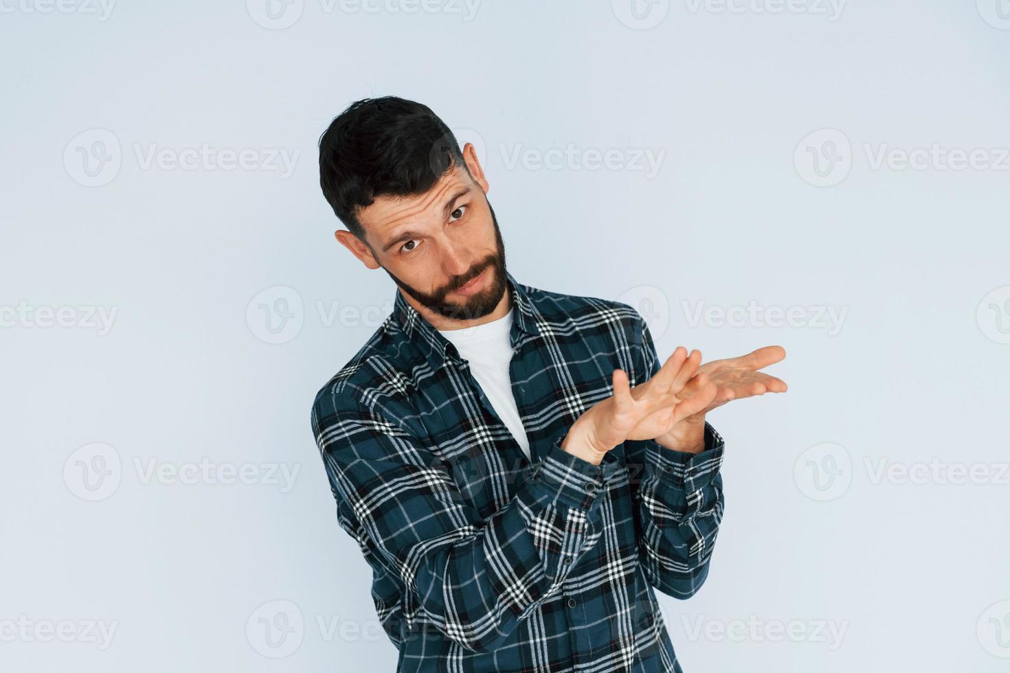 In in a plaid shirt. Young man in casual clothes standing indoors in the studio photo