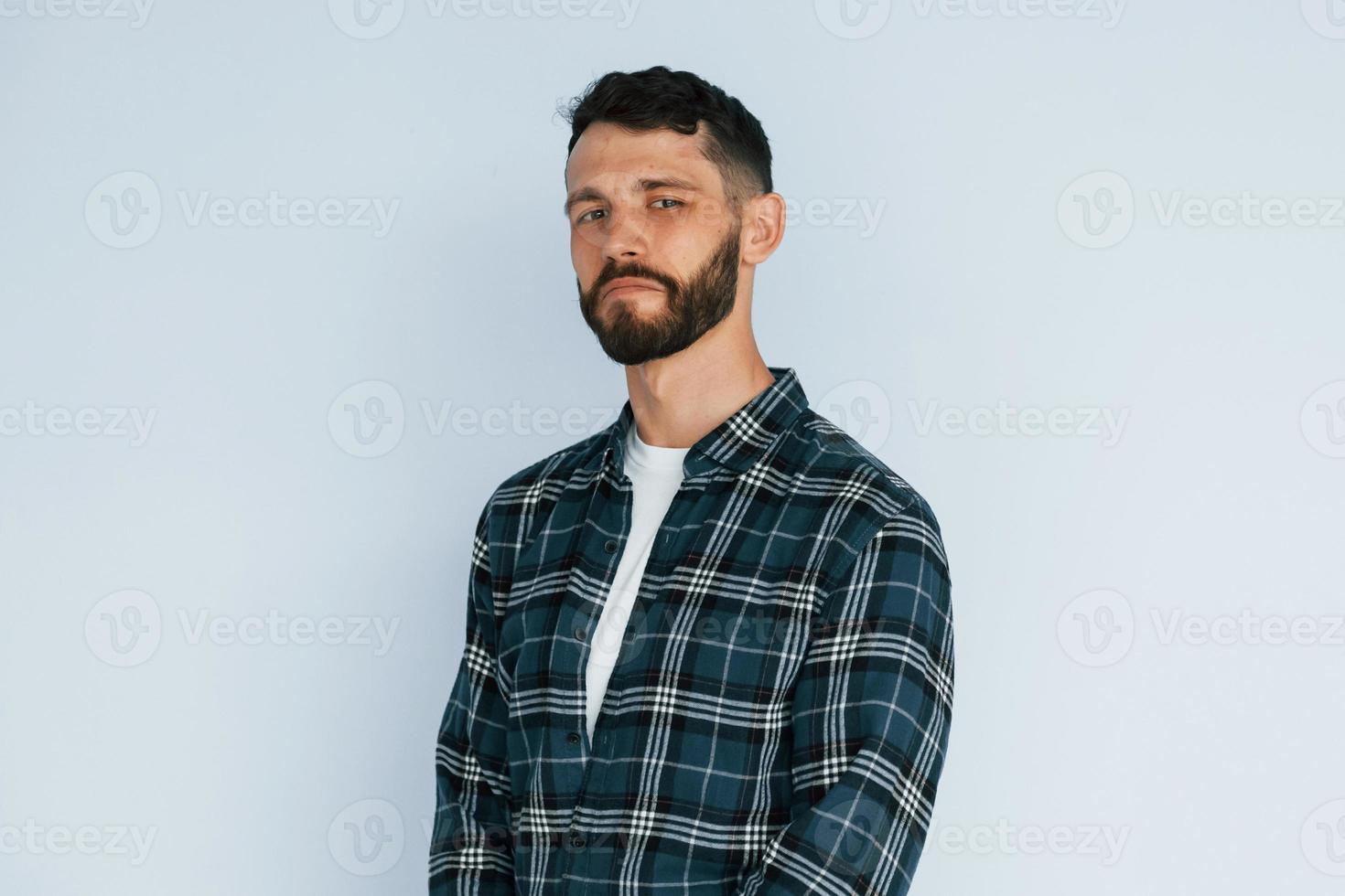 Young man in casual clothes standing indoors in the studio against blye background photo