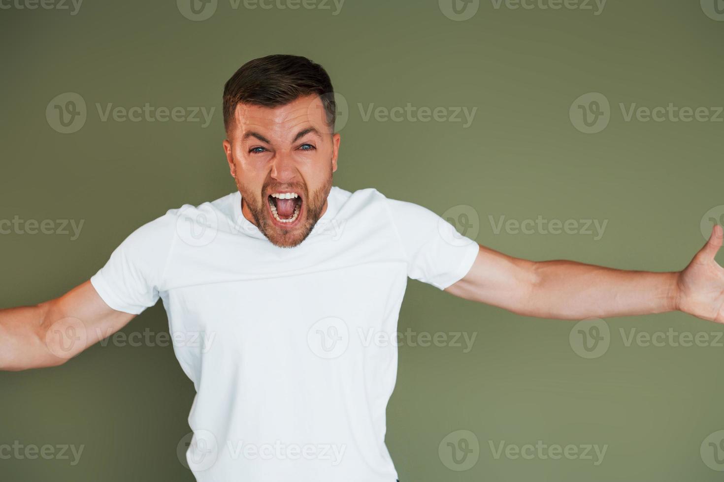 Angry young man in casual clothes standing indoors in the studio photo