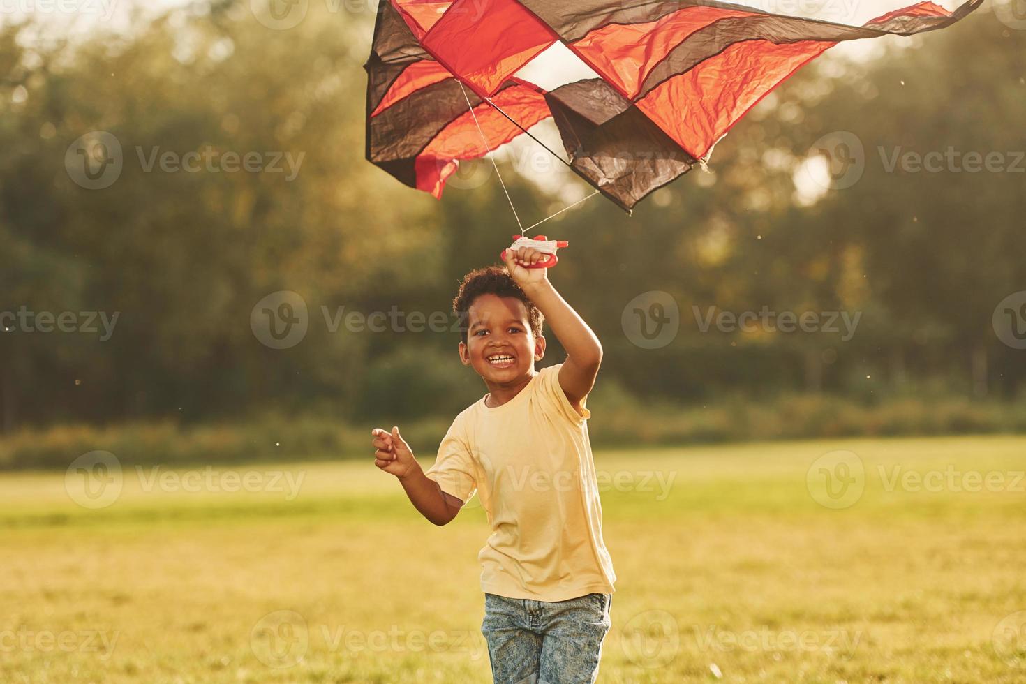 Running with red kite. African american kid have fun in the field at summer daytime photo