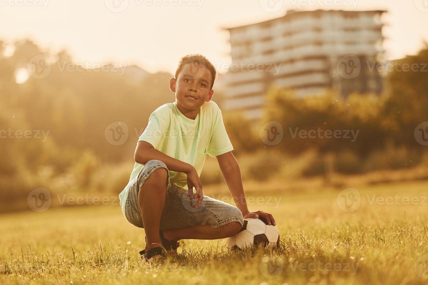 Taking a break. With soccer ball. African american kid have fun in the field at summer daytime photo