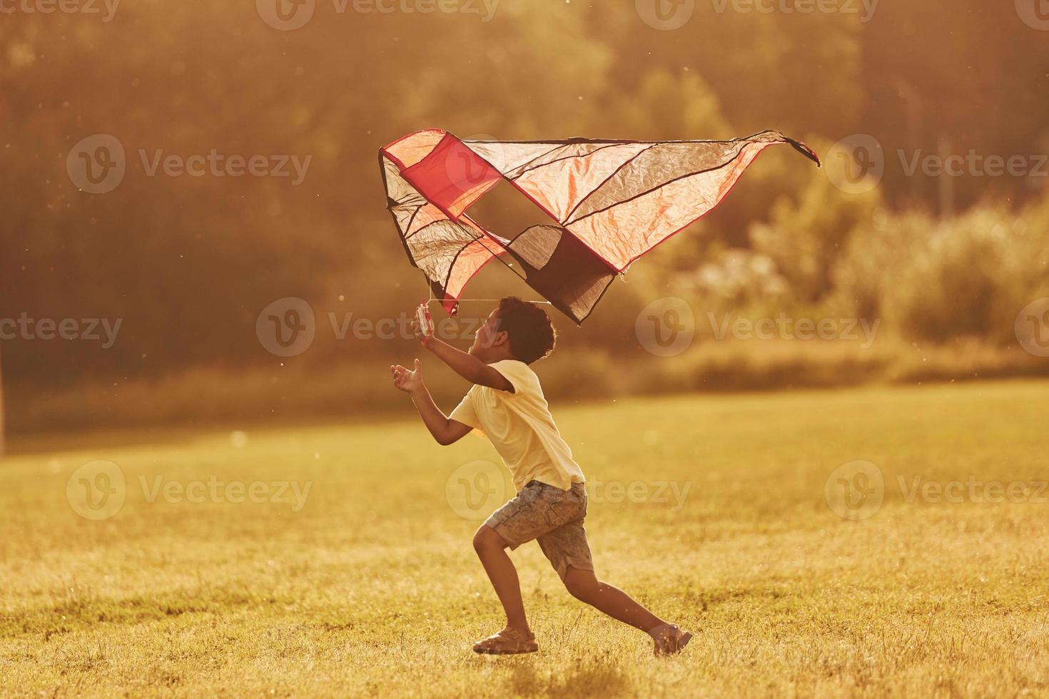 Running with red kite. African american kid have fun in the field at summer daytime photo