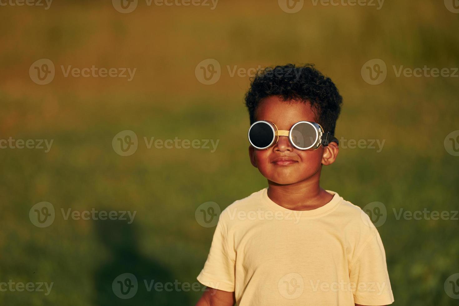 With pilot sunglasses. African american kid have fun in the field at summer daytime photo