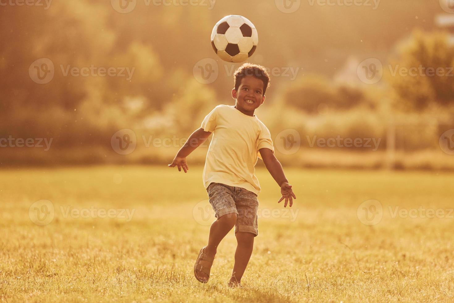 Plays soccer. African american kid have fun in the field at summer daytime photo