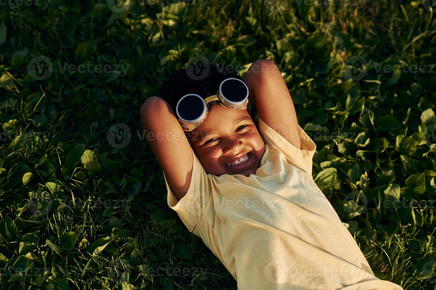 Lying down on the grass. African american kid have fun in the field at summer daytime photo