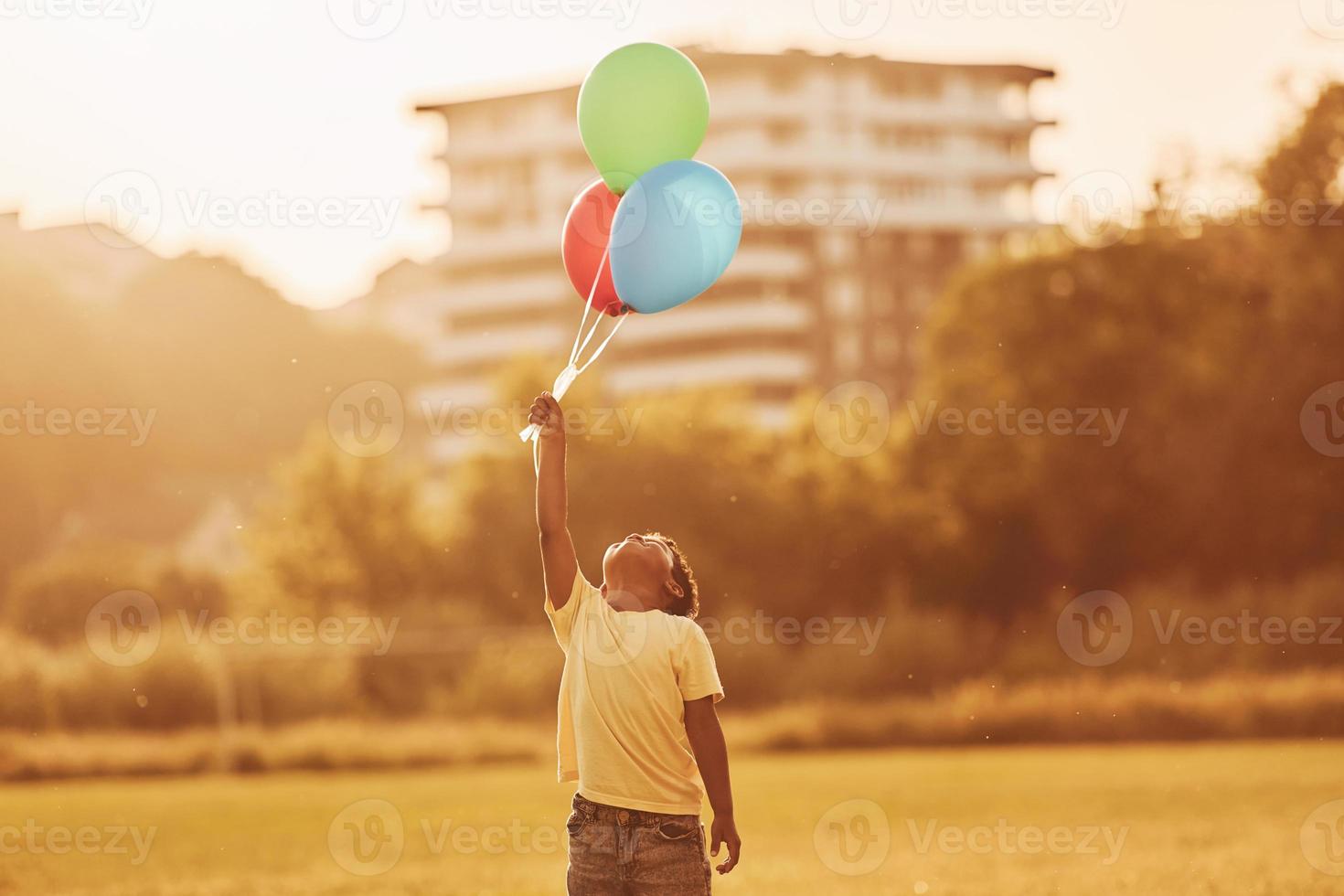 With balloons in hands. African american kid have fun in the field at summer daytime photo