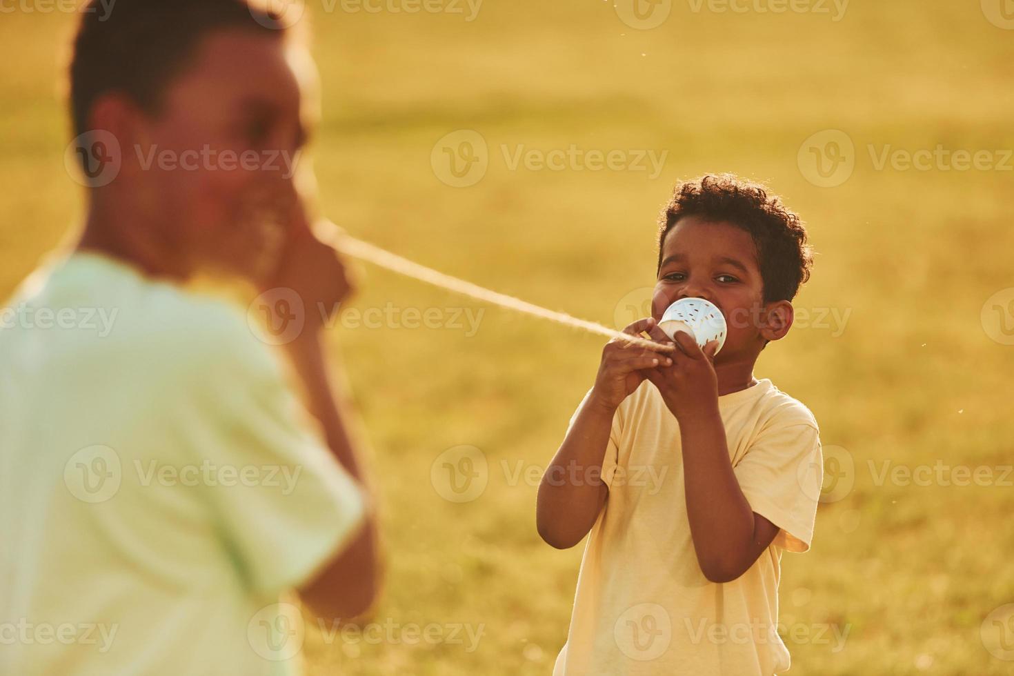 Having conversation by using cups on the knots. Two african american kids have fun in the field at summer daytime together photo