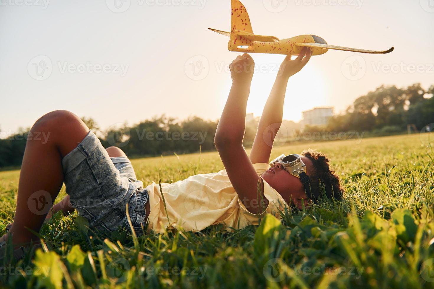 Boy with toy plane. African american kid have fun in the field at summer daytime photo