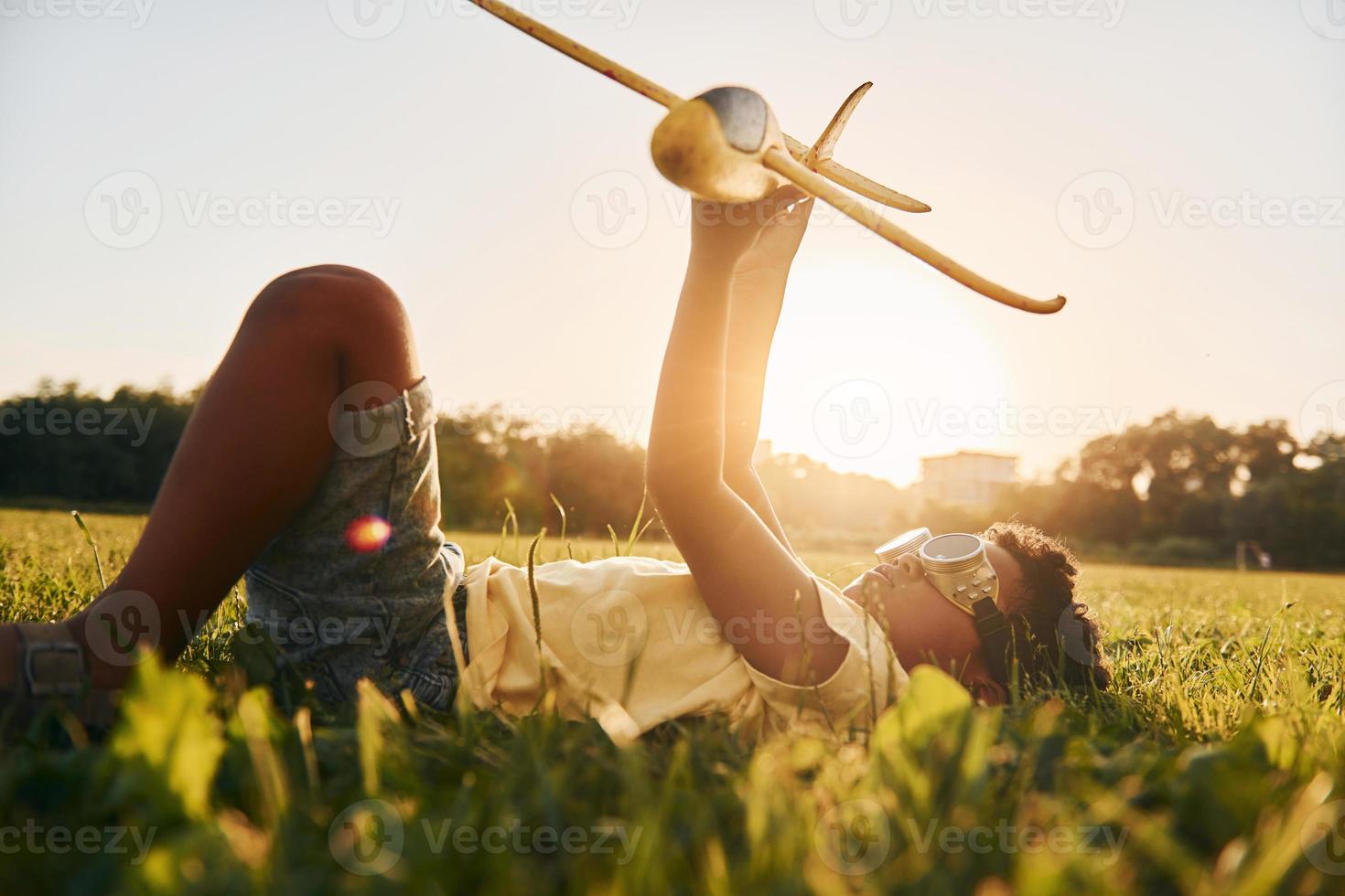 In glasses with toy plane. African american kid have fun in the field at summer daytime photo
