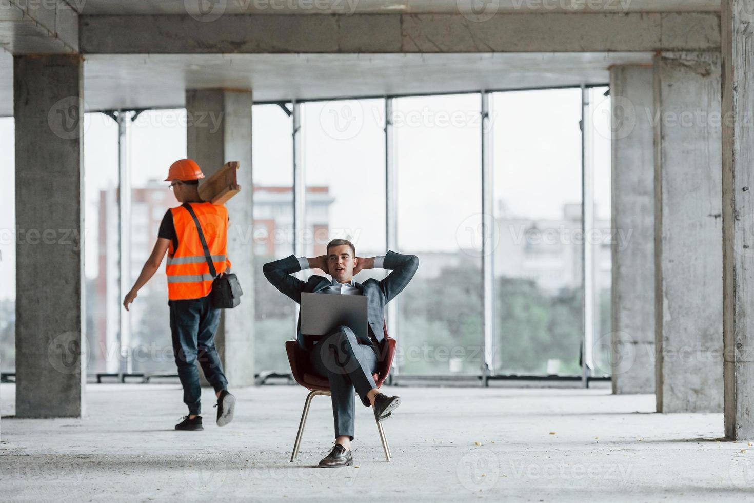 Moving object. Man in suit and handyman in orange protective wear is working on construction photo