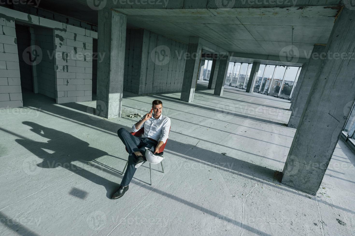 Successful young man in formal wear is working indoors on the construction photo