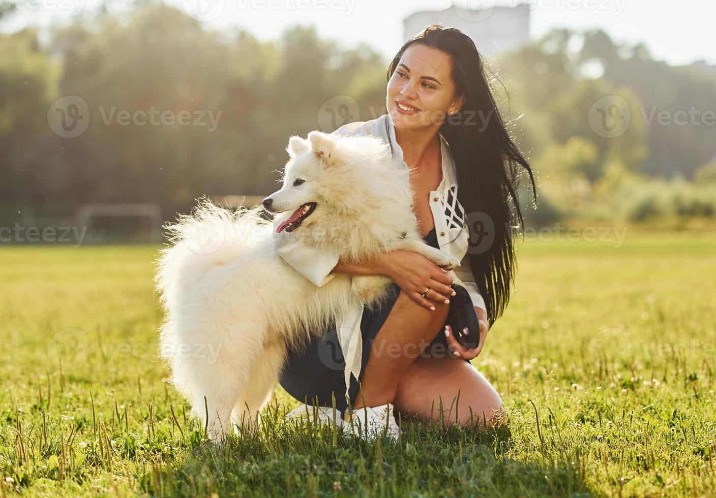 Woman is sitting on the ground of field with her cute dog photo