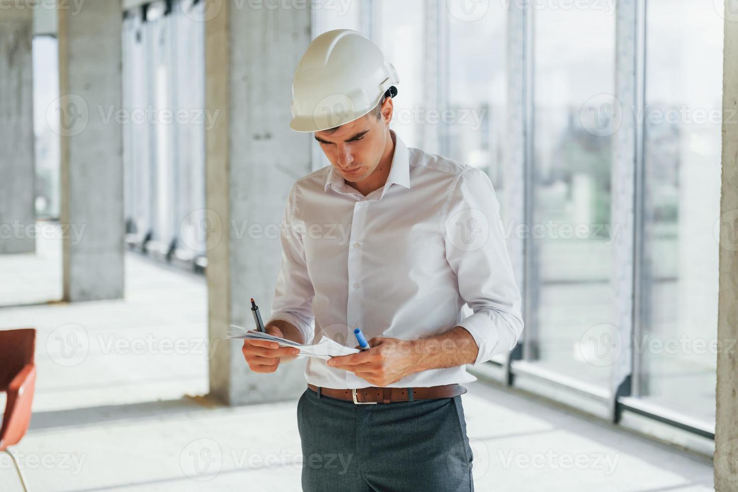 Holds documents. Young man in formal wear is working indoors on the construction photo
