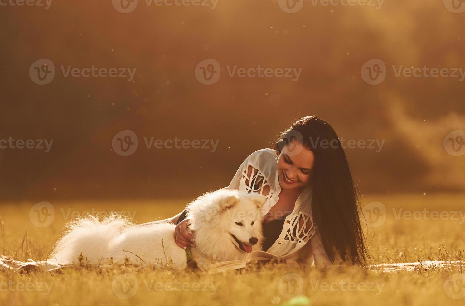 Laying down on the ground. Woman with her dog is having fun on the field at sunny daytime photo