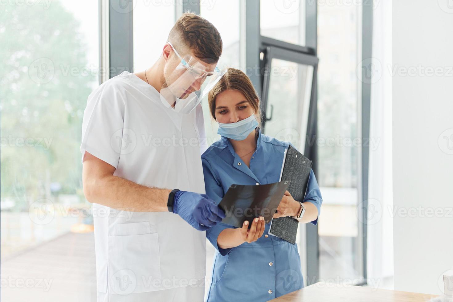 Looking at documents. Two doctors in uniform standing indoors and working together photo