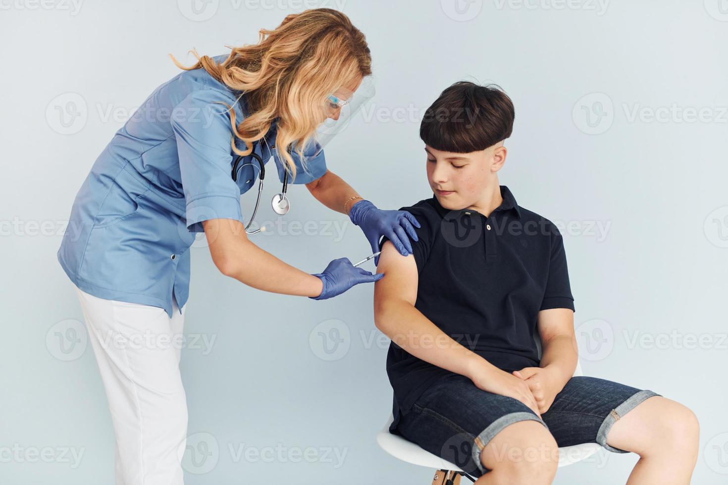 Doctor in uniform making vaccination to the boy in black shirt photo