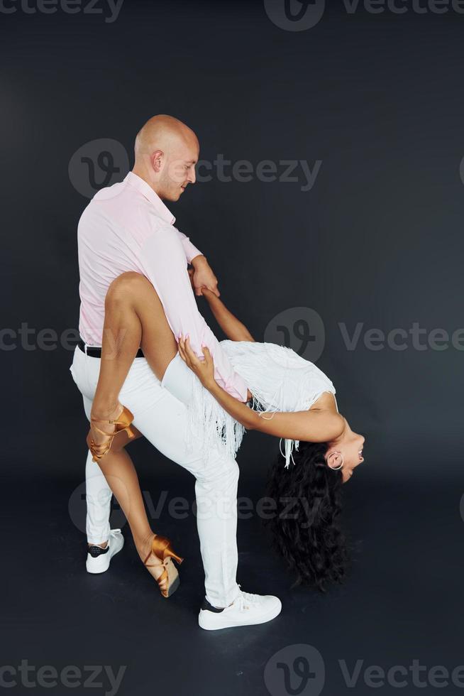 Dancing against black background. Cheerful couple is together indoors photo