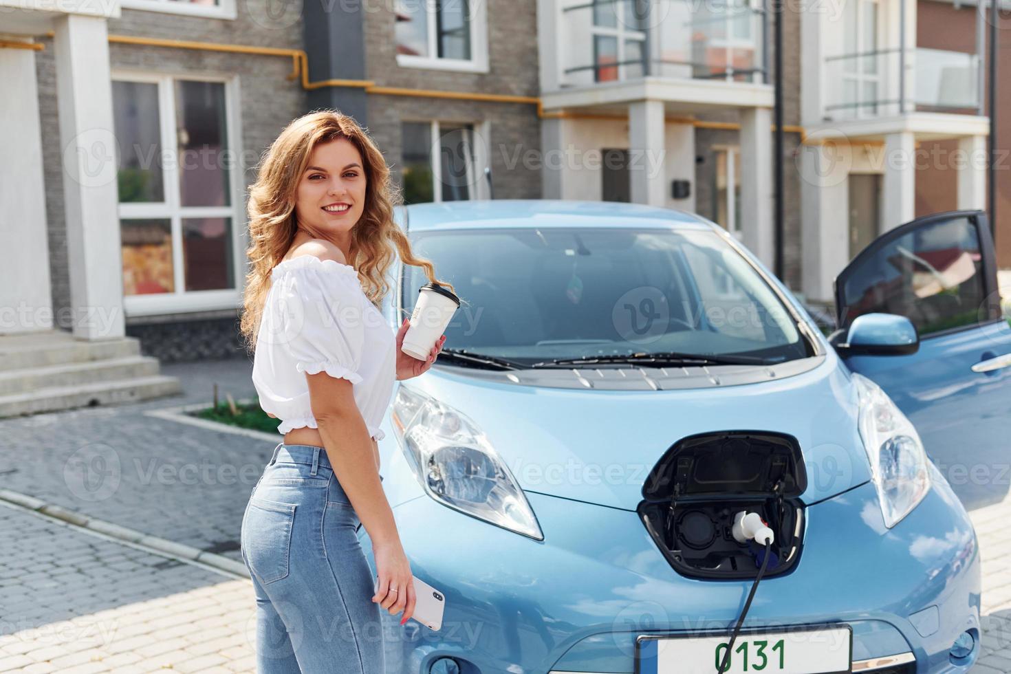 With cup of drink. Young woman in casual clothes with her electromobile outdoors at daytime photo