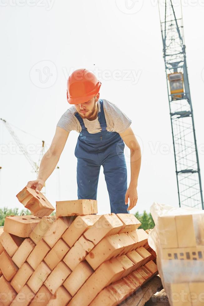 sosteniendo ladrillos. joven trabajador de la construcción en uniforme está ocupado en el edificio sin terminar foto