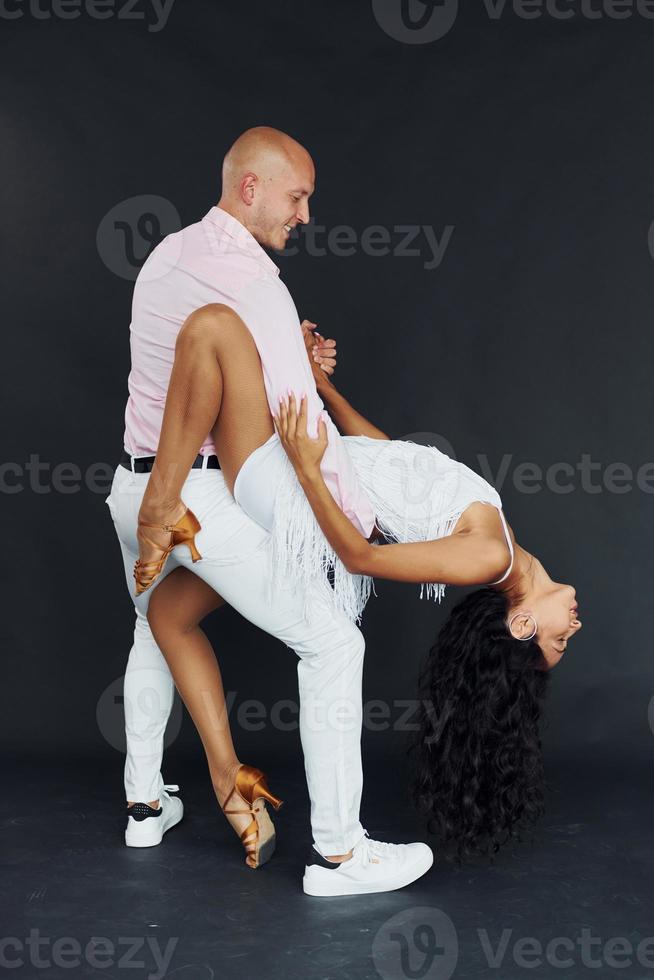 Dancing against black background. Cheerful couple is together indoors photo