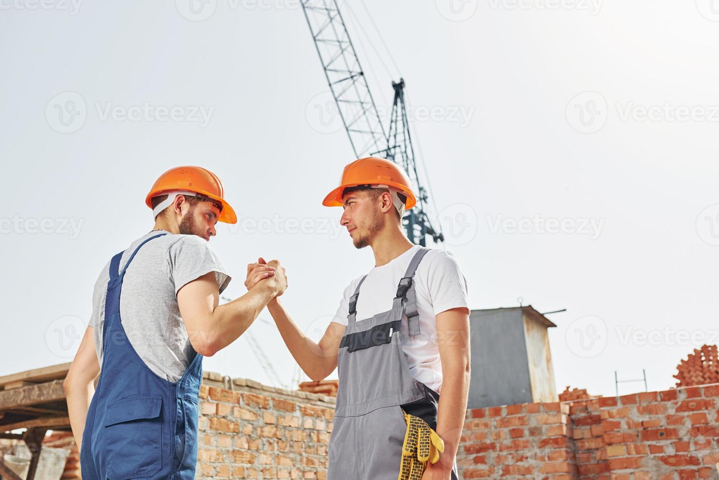 Two young construction workers in uniforms is busy at the unfinished building photo