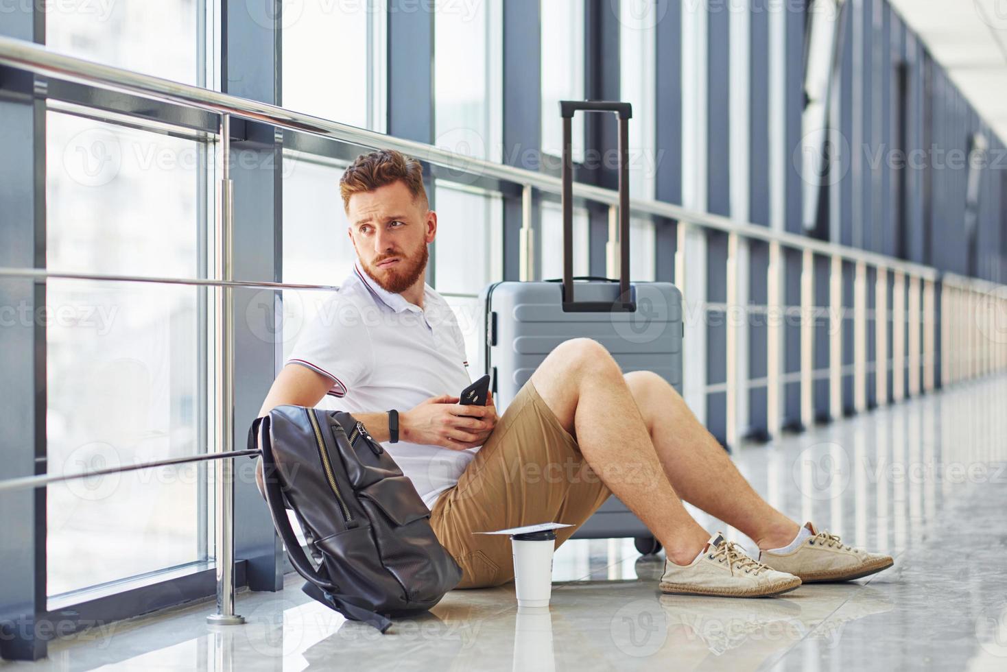 Man is on the ground. Young traveler is on the entrance hall in the airport photo