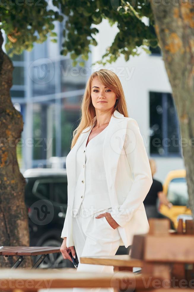 Near table. Woman in formal wear standing outdoors in the city at daytime photo