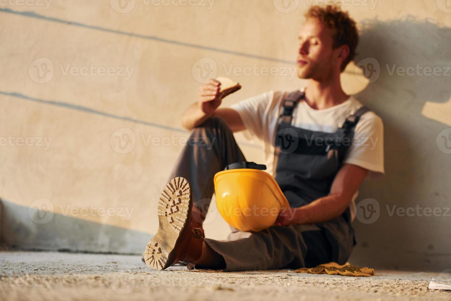 Eating food. Young man working in uniform at construction at daytime photo