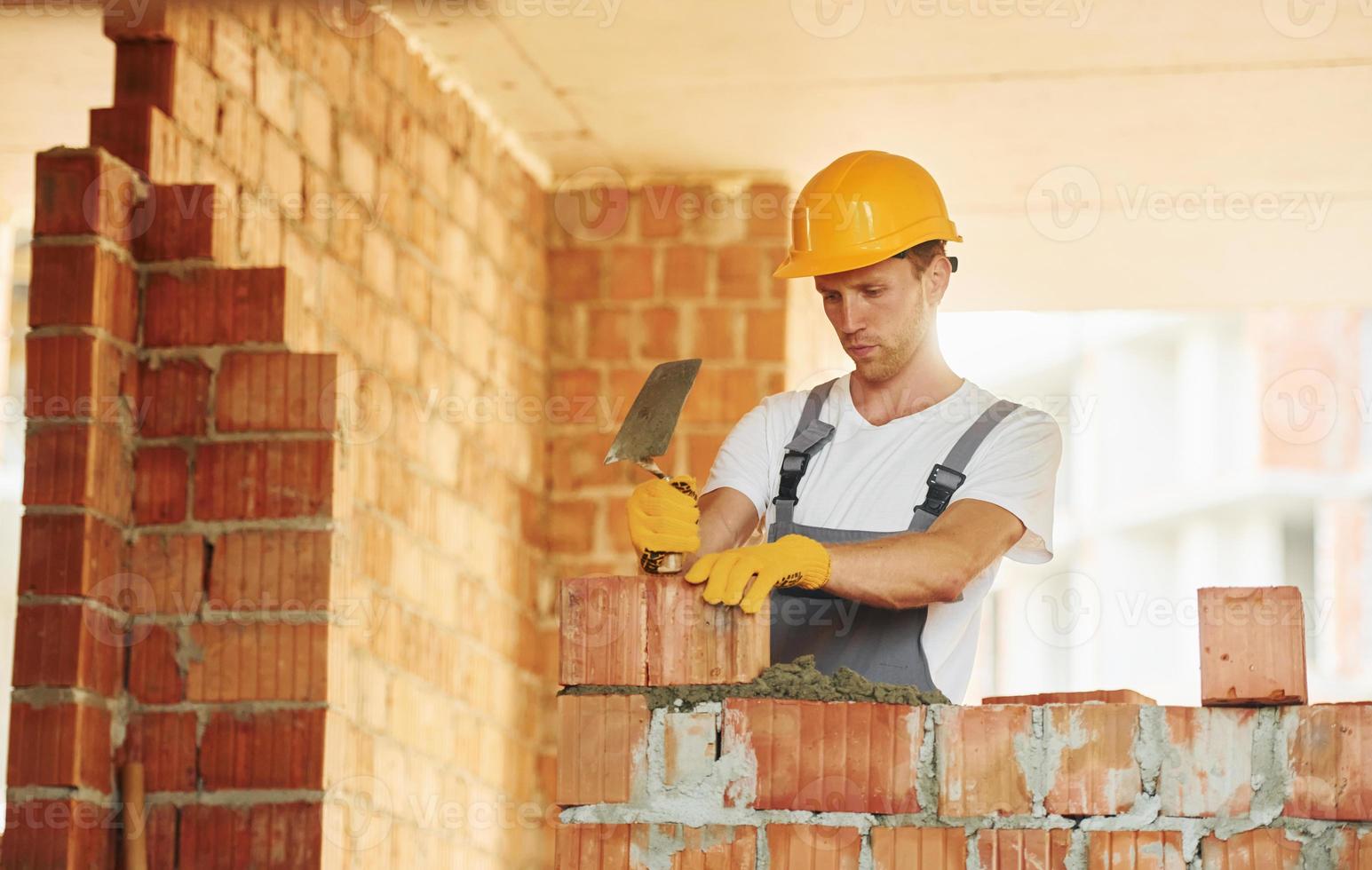 Bricks installation. Young man working in uniform at construction at daytime photo