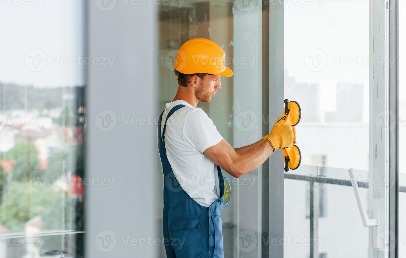 Clearing windows. Young man working in uniform at construction at daytime photo