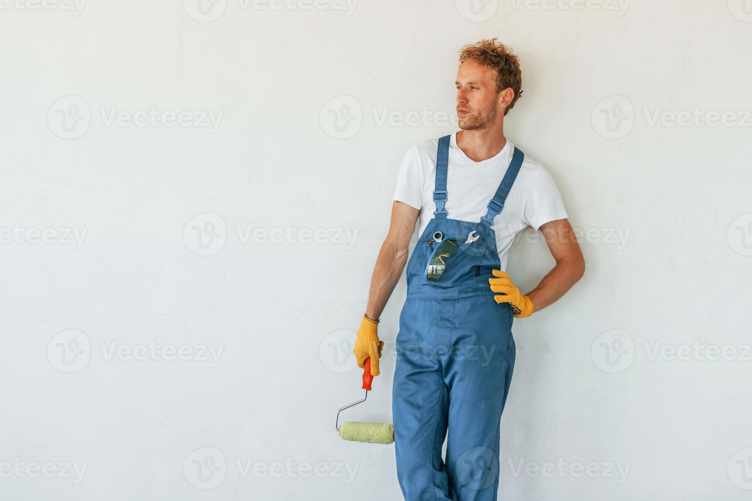 Standing against finished white walls. Young man working in uniform at construction at daytime photo