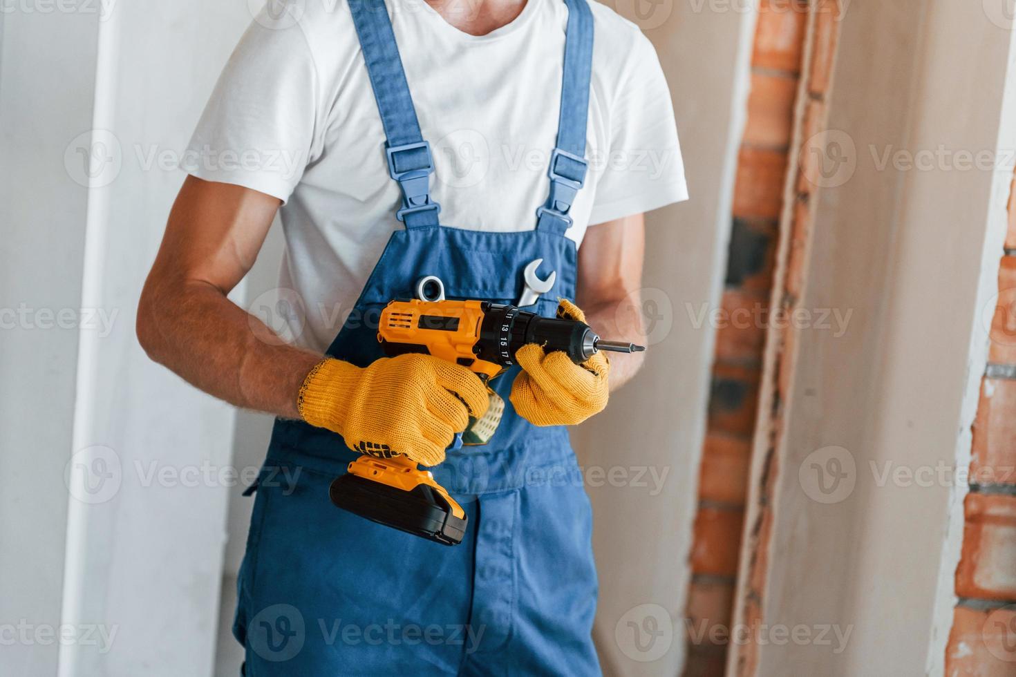 Empty walls. Young man working in uniform at construction at daytime photo