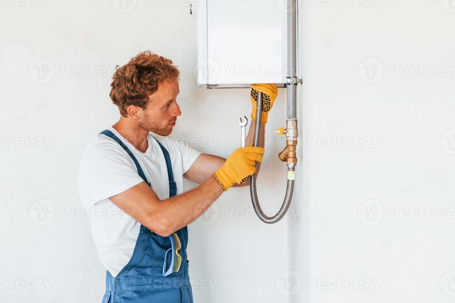Repairing water heater. Young man working in uniform at construction at daytime photo