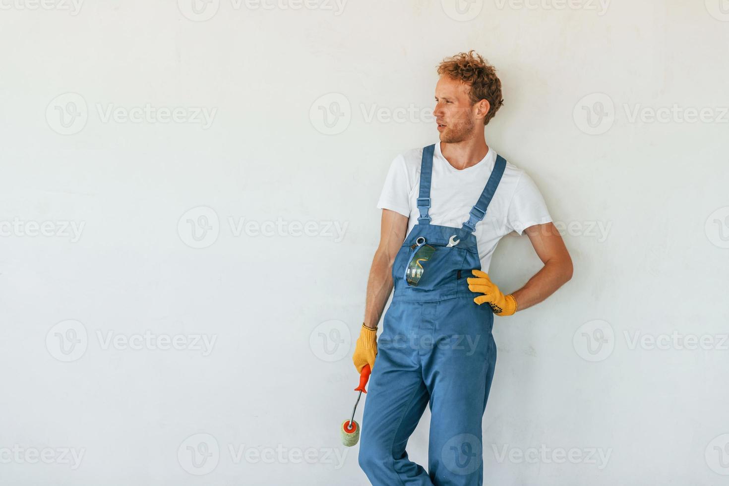 Against white walls. Young man working in uniform at construction at daytime photo