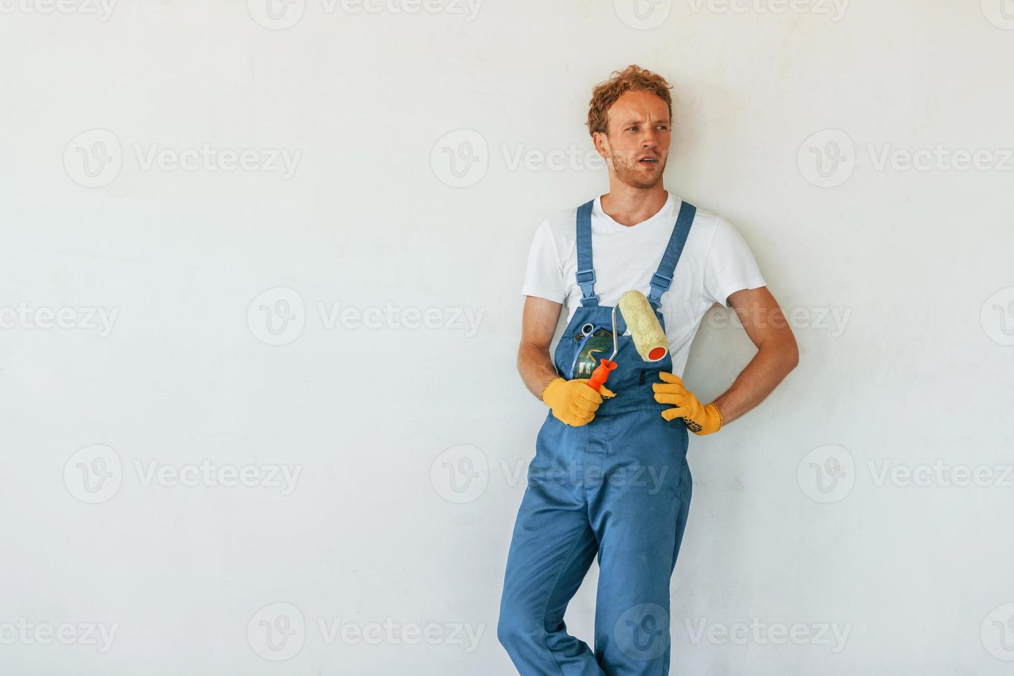 Against white walls. Young man working in uniform at construction at daytime photo