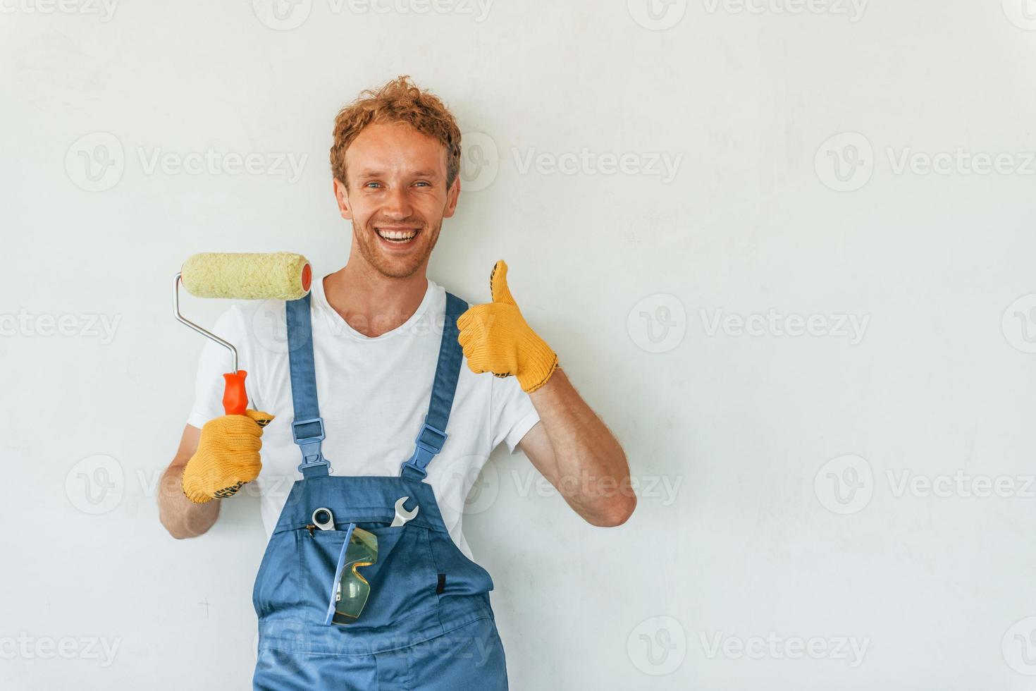 Against white walls. Young man working in uniform at construction at daytime photo