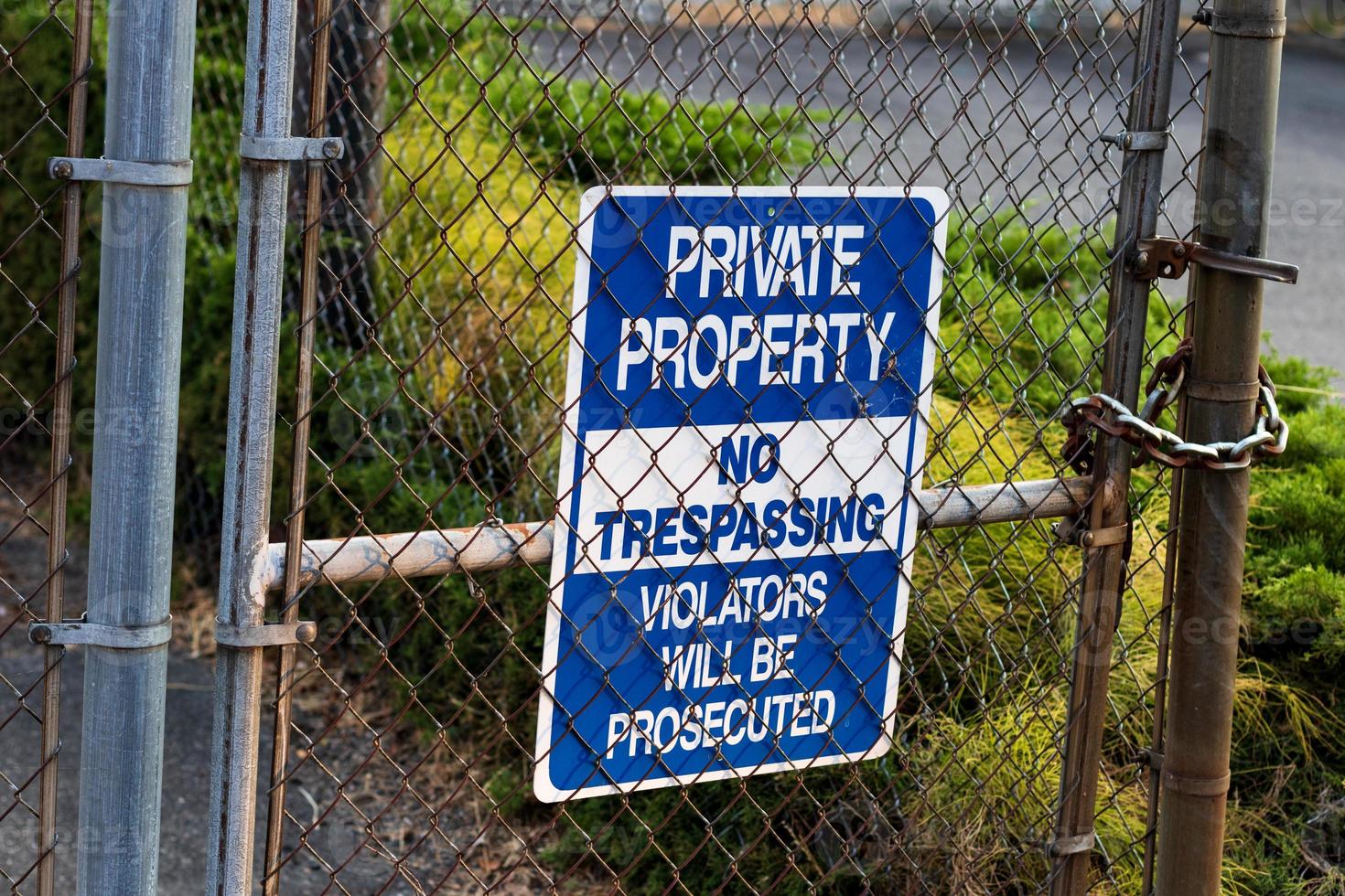 Blue private property no trespassing sign on a chain link fence photo