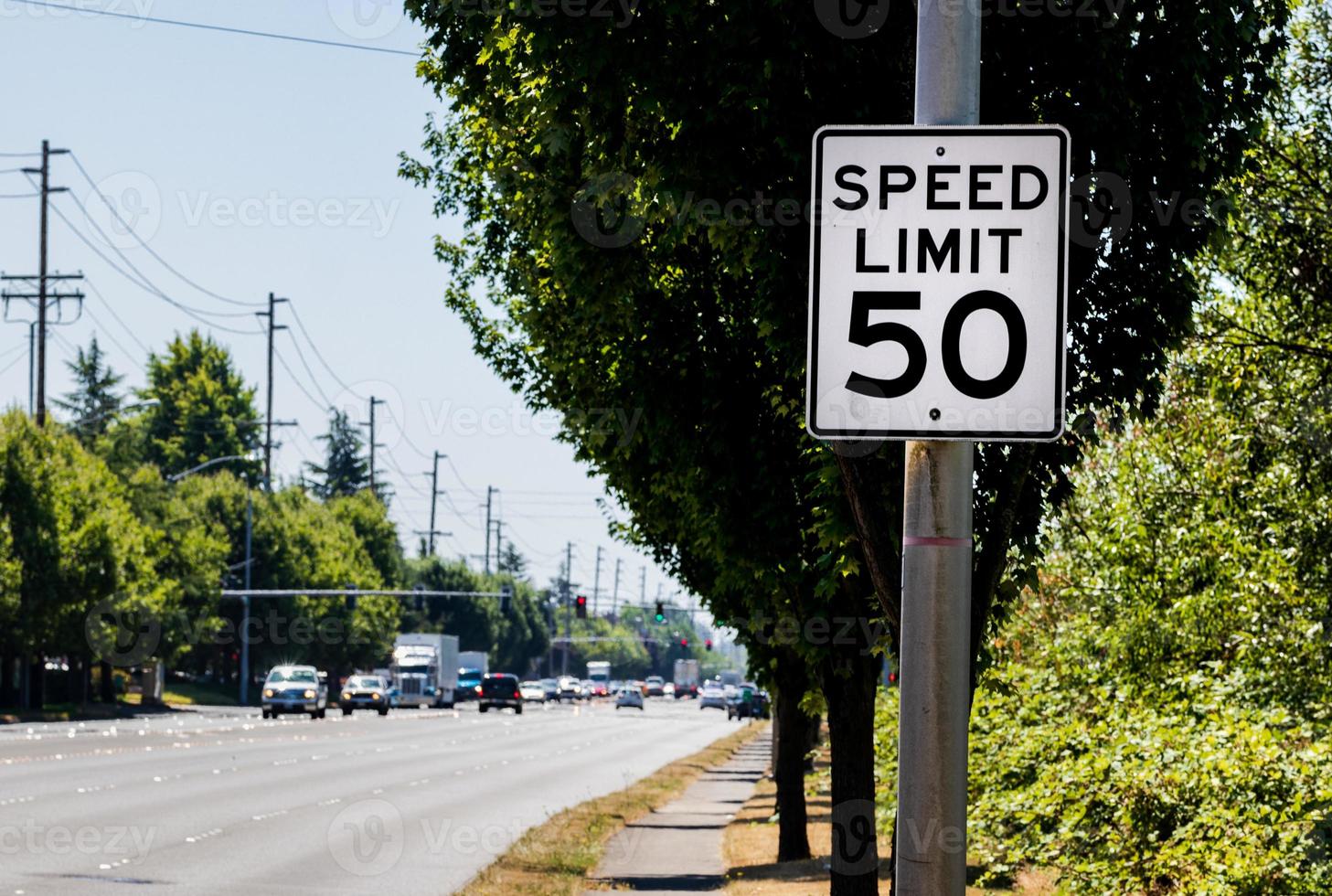 50 mph speed limit sign on post with a road and tree photo