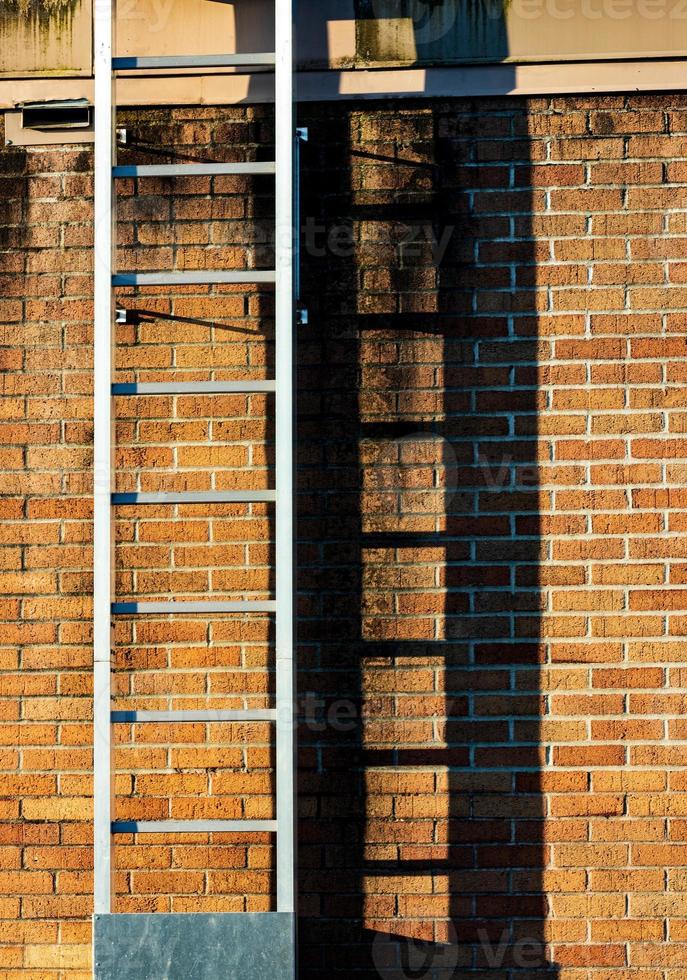 Ladder casting shadow on a worn old stained brick wall photo