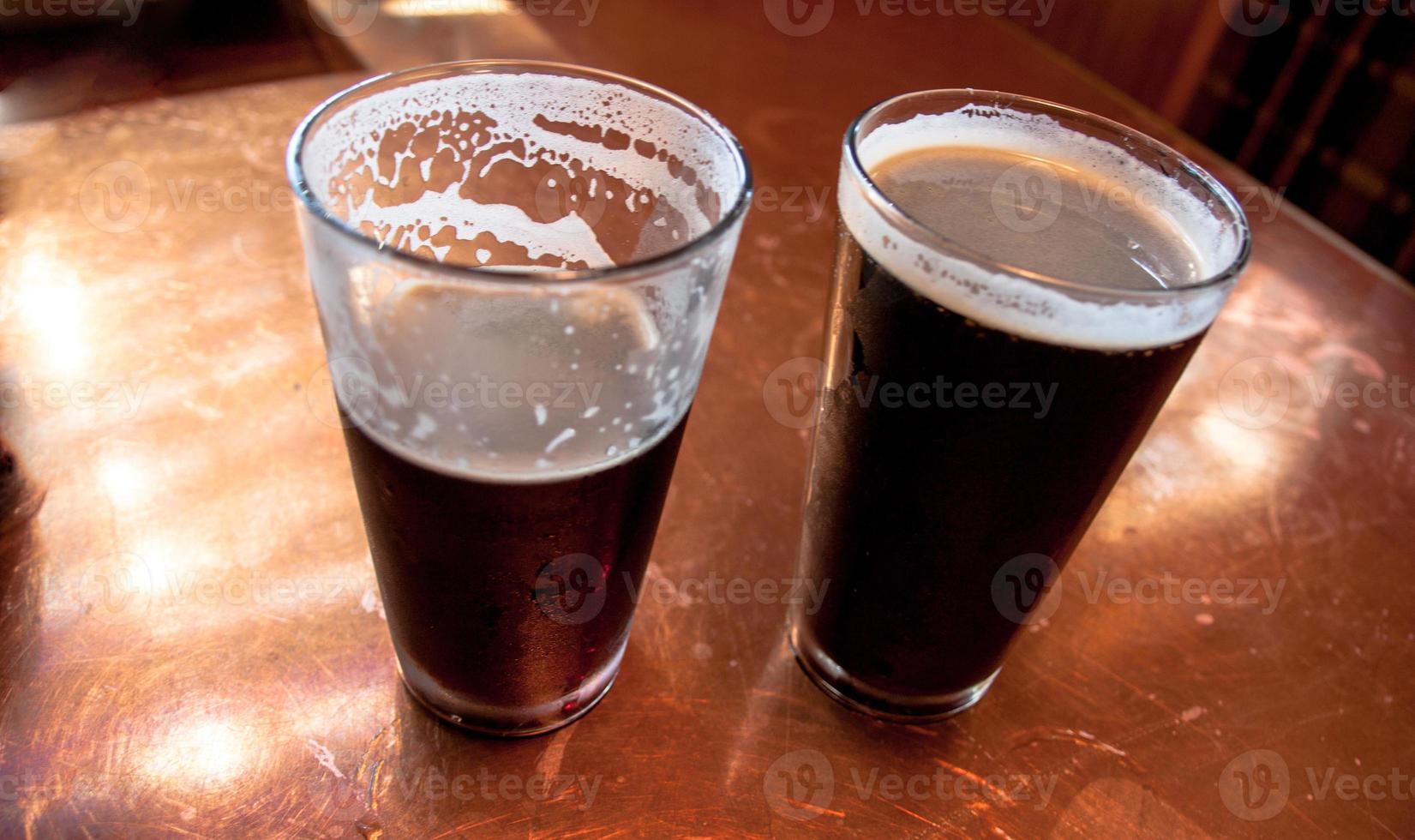 2 tall glasses of dark beer on a copper top table photo