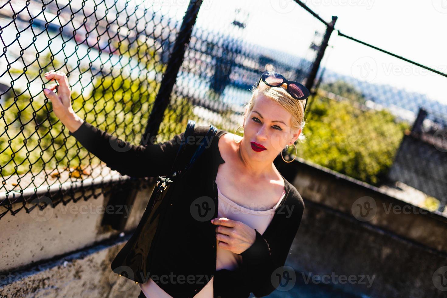 Attractive blonde woman standing on a city sidewalk next to a fence. photo