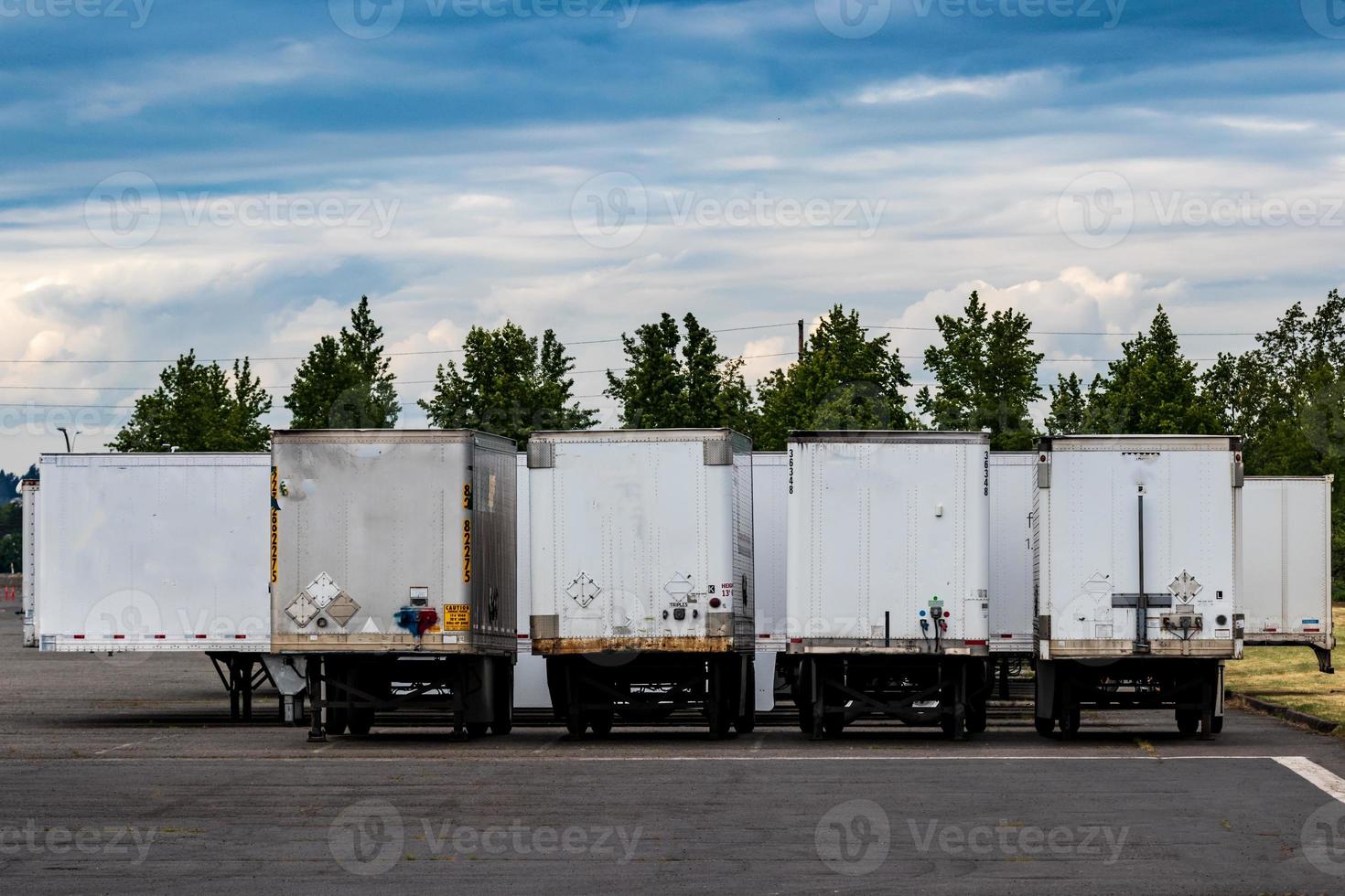 Semi tractor trailers parked in a row with doors closed under a blue cloudy sky photo