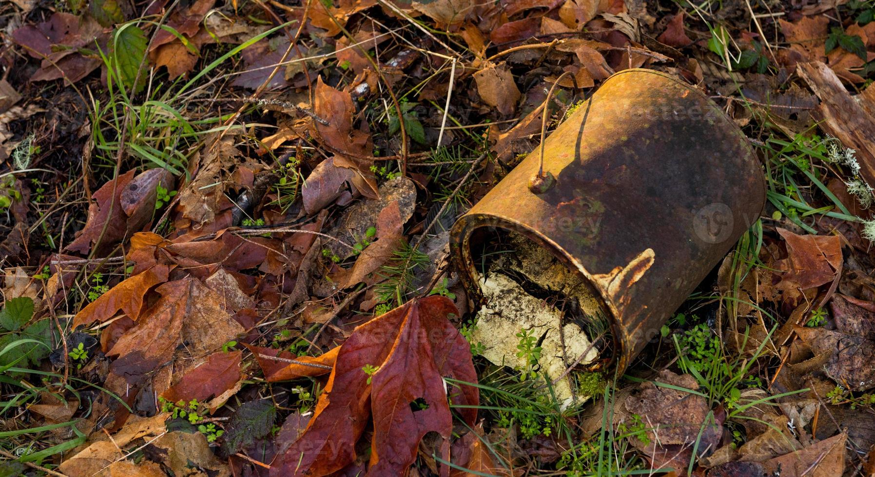 Old rusty paint can lying on the forest floor surrounded by leaves photo